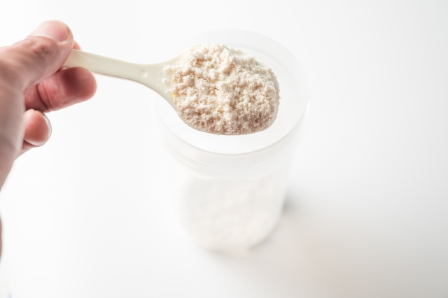 スプーンですくったプロテインの粉末を、シェイカーに入れている様子