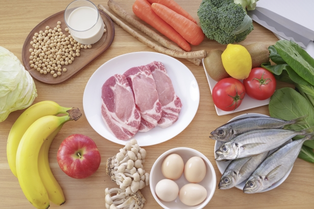 肉、魚、卵、野菜、果物など、栄養バランスの良い食事をイメージさせる様々な食材が、木のテーブルの上に並べられている