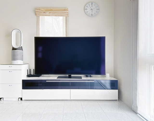 白を基調とした、清潔感のあるモダンなリビングルーム。テレビ台の上に大きなテレビが置かれている。