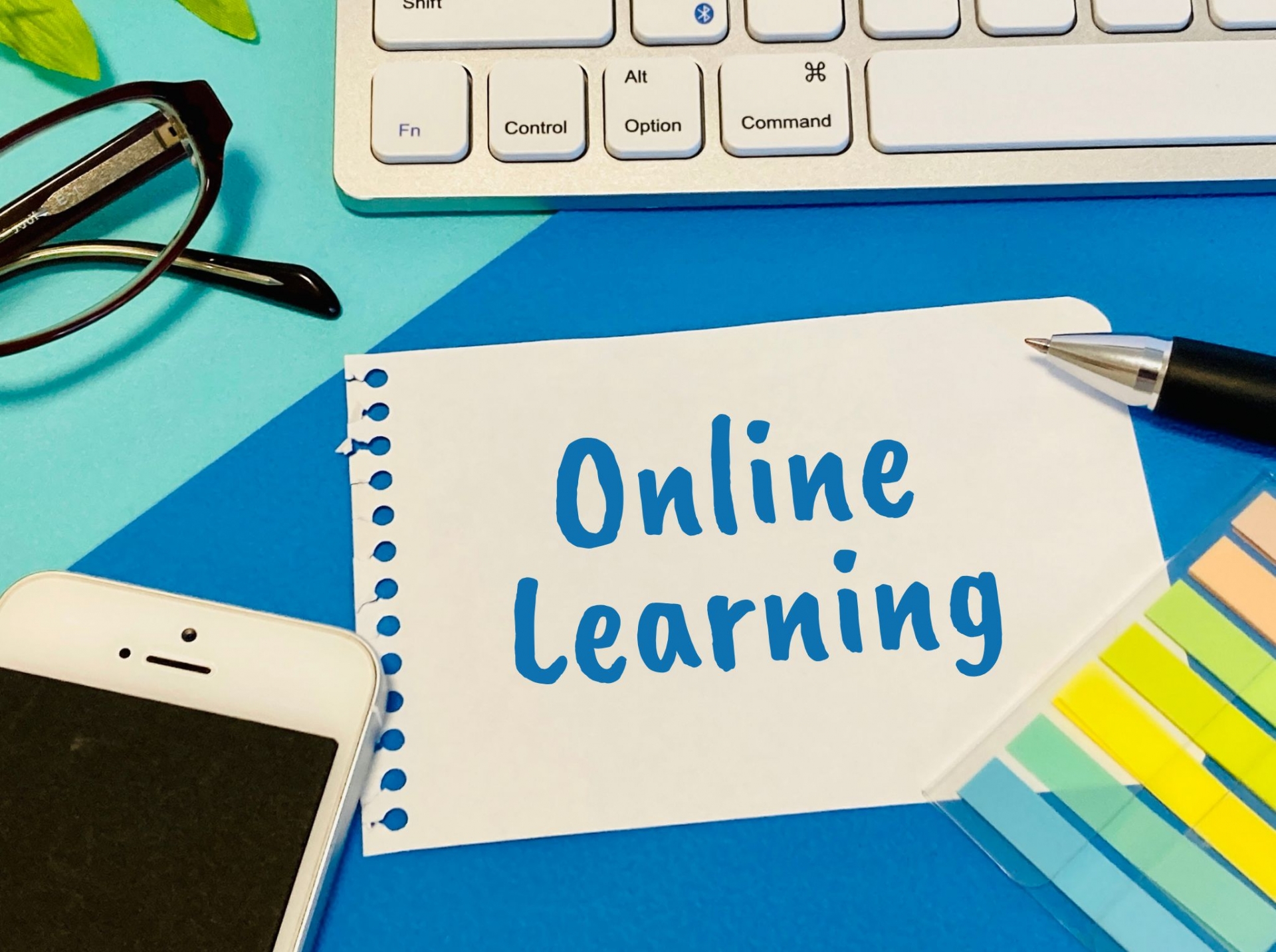 「Online Learning」と手書きされたメモ用紙、キーボード、スマートフォン、ペン、メガネが並んだデスク