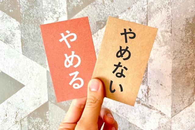 「やめる」と「やめない」と書かれた2枚のカードを持つ手